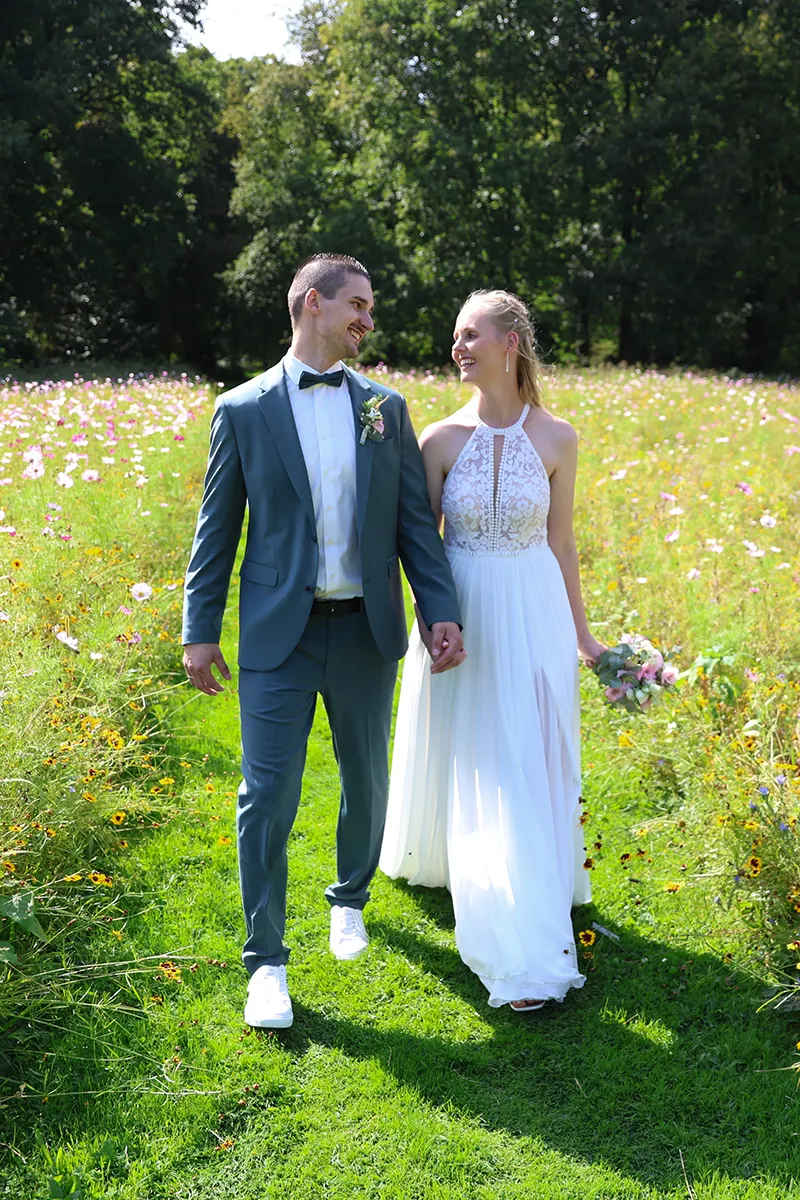 Ein Brautpaar das durch ein Blumenfeld beim Wasserschloss Anholt läuft und sich dabei anlächelt