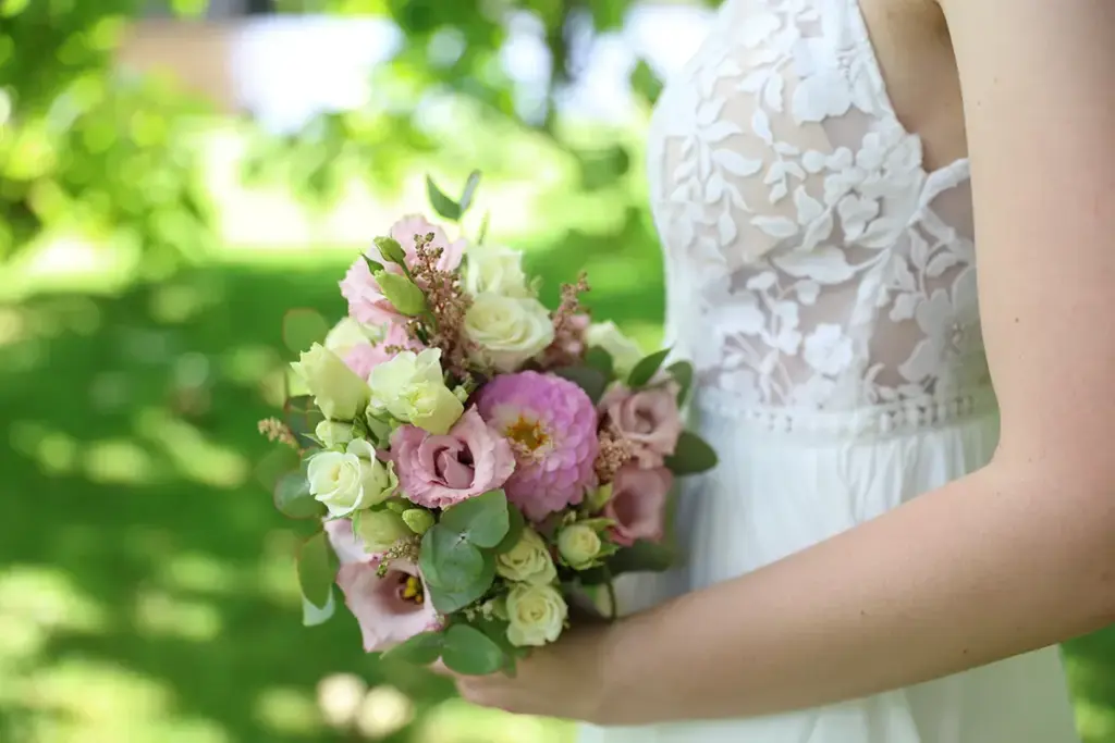 Ein schöner Brautstrauss mit hellen Blumen gehalten vor dem Brautkleid