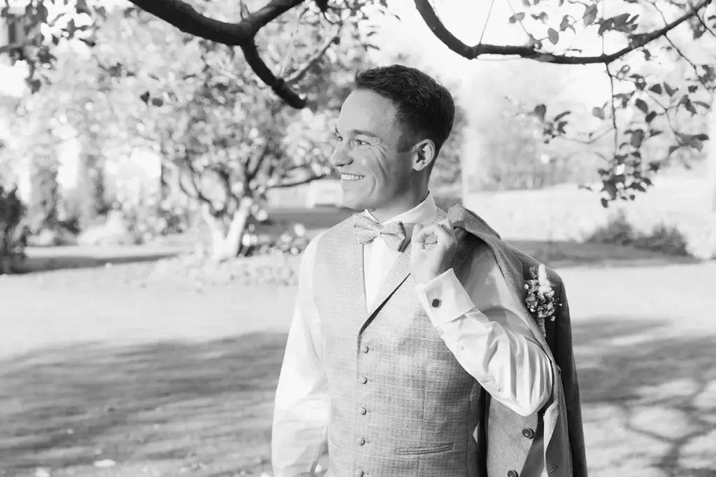 Schwarz-Weiß-Aufnahme vom Bräutigam in Weste unter einem alten Baum