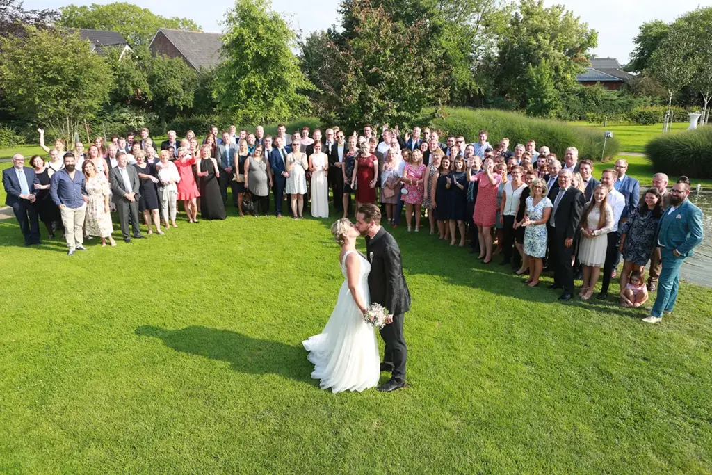 Küssendes Brautpaar mit allen Gästen Gruppenfoto